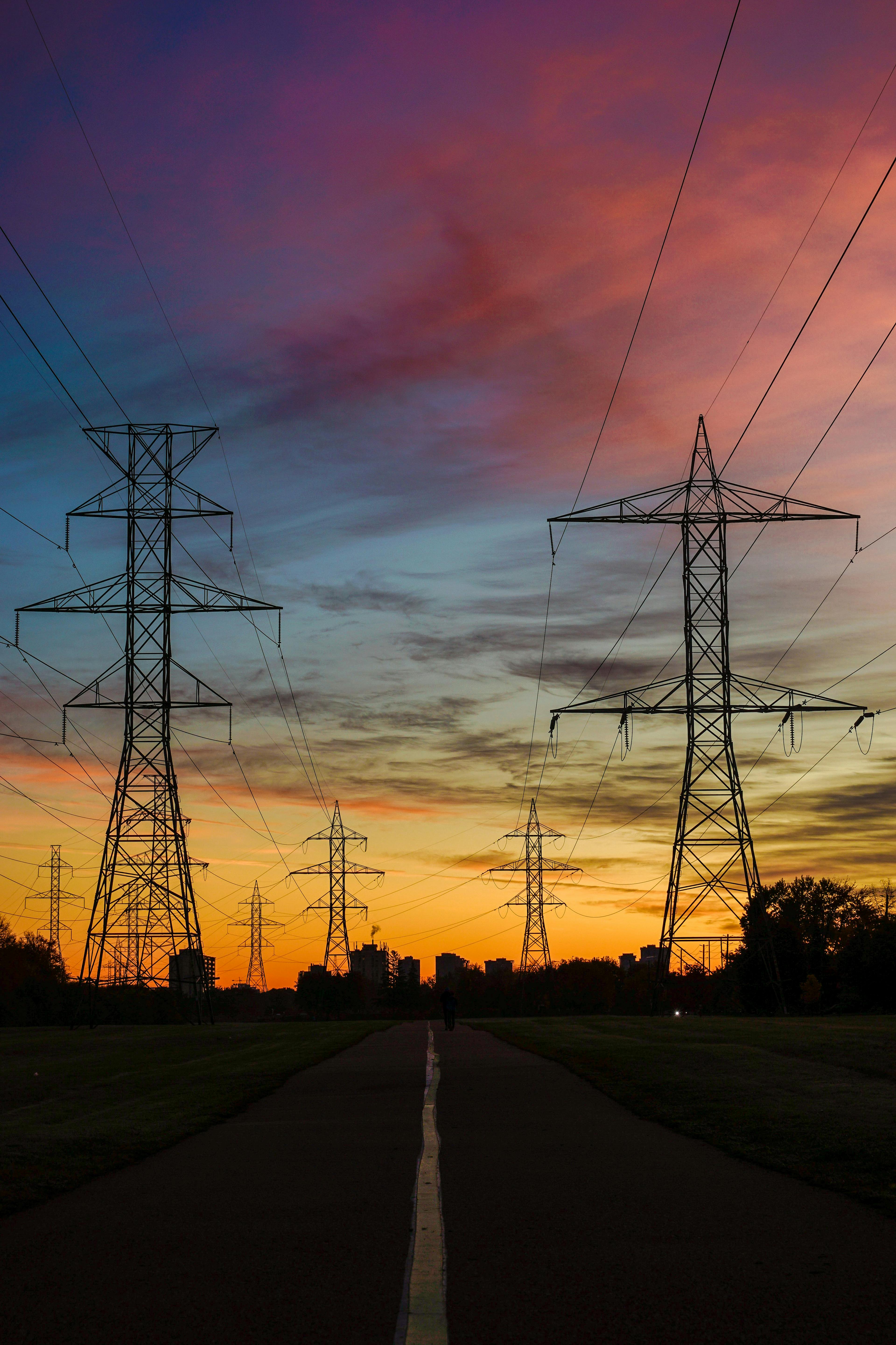 A colorful sky silhouettes power lines and towers at sunset, creating a dramatic view.