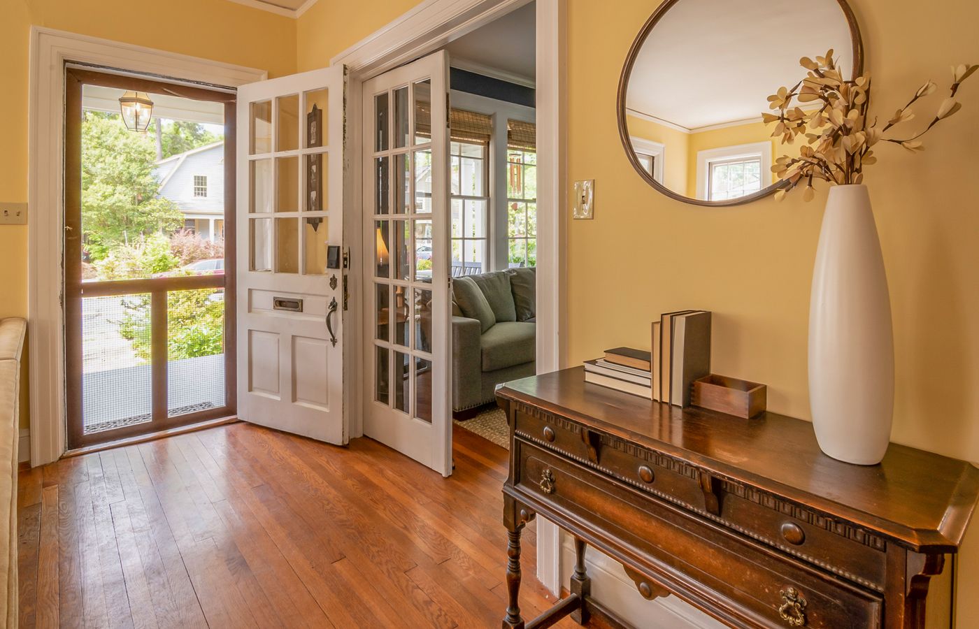 Sunlit entryway featuring a wooden dresser, mirror, and vase with decorative branches.