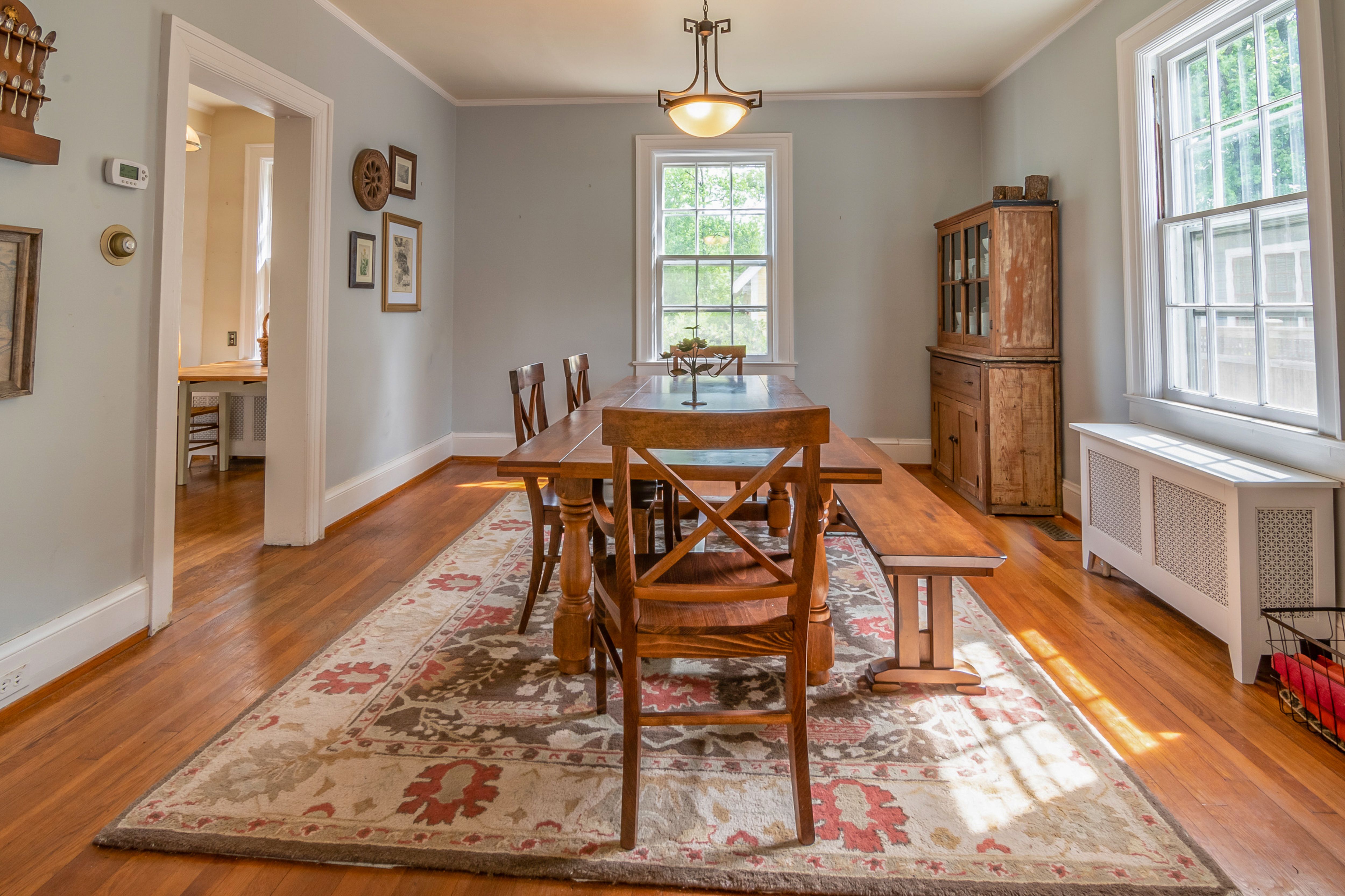 Dining room with wooden table, chairs, patterned rug, and large windows in a bright, traditional interior.