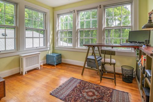 Free Spacious home office featuring a wooden desk, large windows, and natural light in a serene setting. Stock Photo