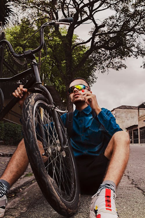 Man sitting on ground near bicycle in park on cloudy day