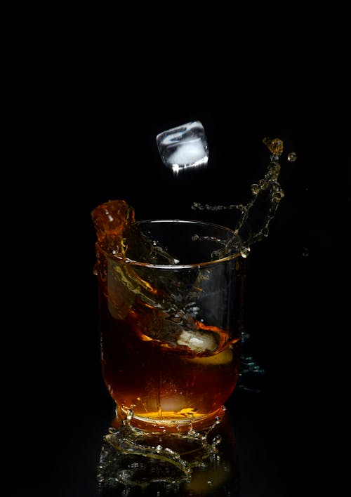 Free Liquid Splashing Out of a Glass and a Flying Ice Cube Stock Photo