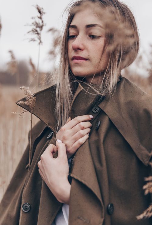 Free A young woman in a brown trench coat stands in a serene autumn field, exhibiting calm strength. Stock Photo