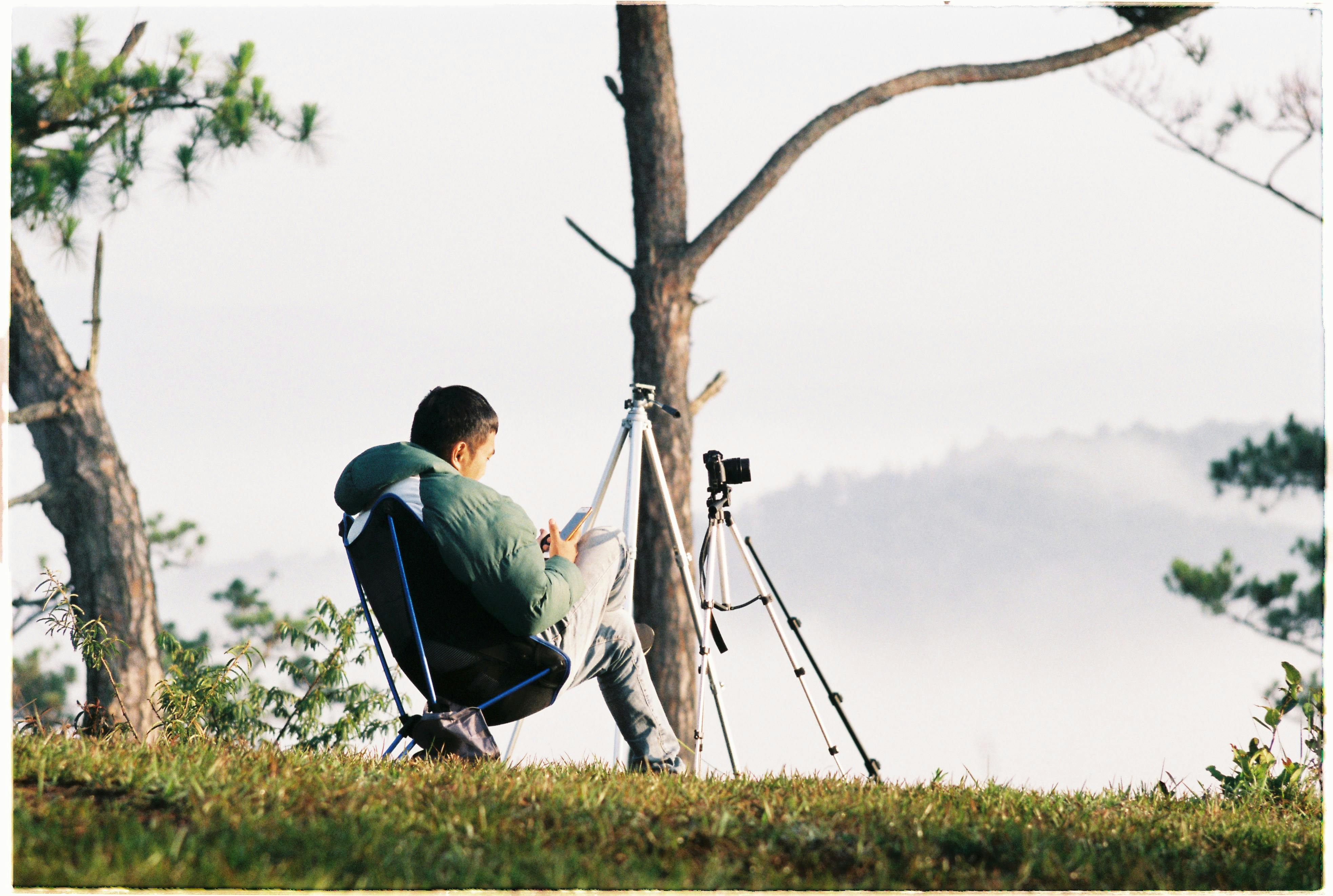 A man sits with a camera and tripod, capturing serene outdoor scenery.