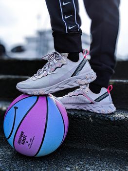 Close-up of white sneakers on a colorful basketball on outdoor steps.