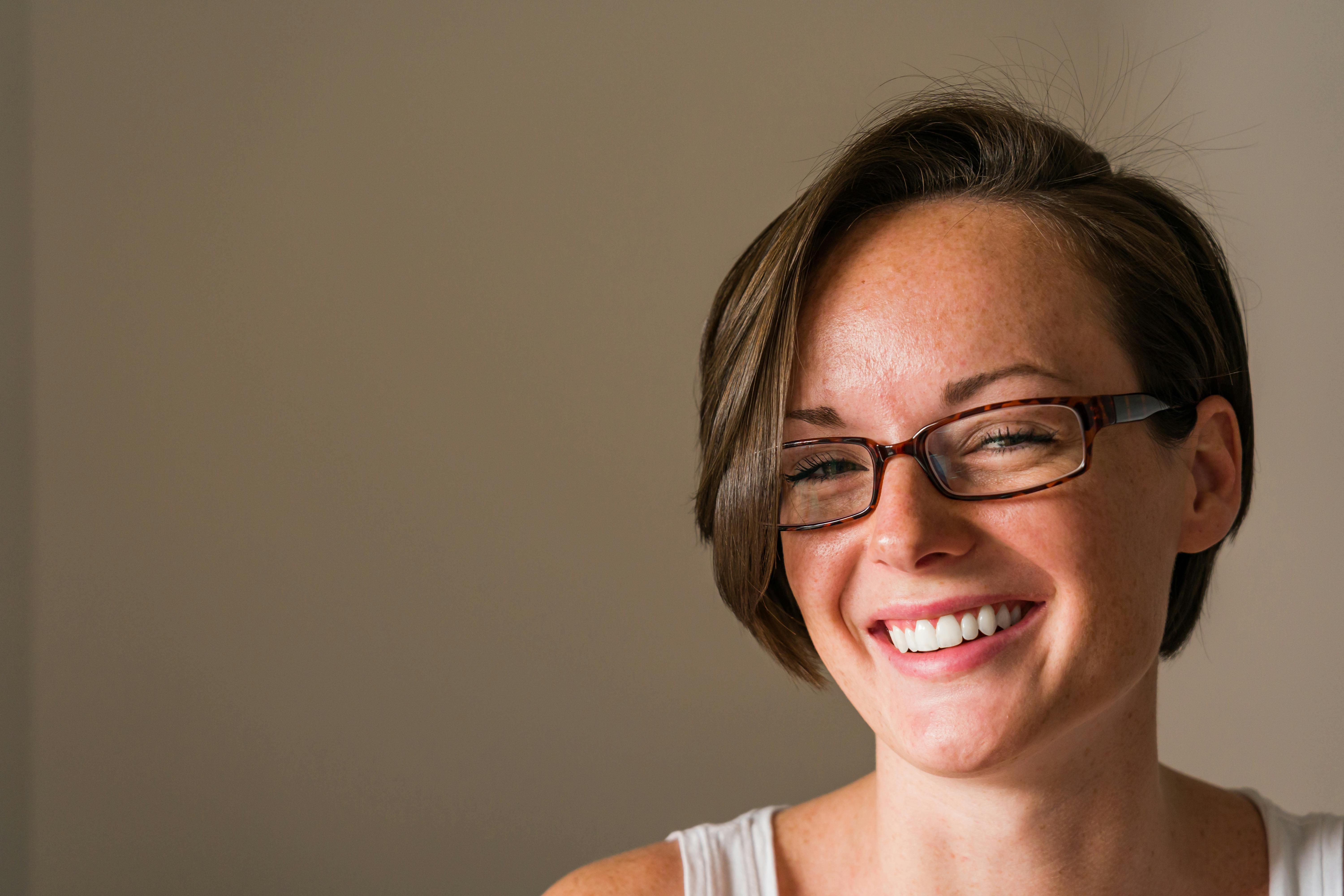 一位开朗的短发女子戴着眼镜，在室内热情微笑，散发着积极的情绪