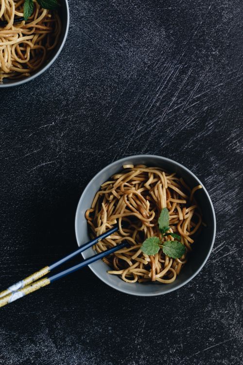 Free Top view of Asian noodles in a bowl with chopsticks on a dark surface, garnished with herbs. Stock Photo