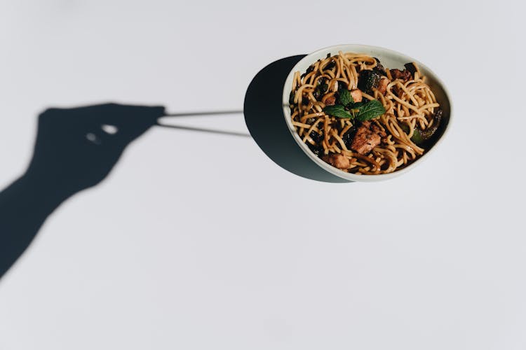 Shadow Of Hand With Chopsticks Reaching To Bowl Of Noodles