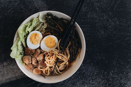 A vibrant ramen bowl with chopsticks, noodles, eggs, and vegetables, captured in a top view.