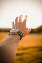 Crop unrecognizable male traveler with wristwatch reaching out to sun while relaxing in countryside