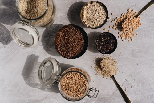 Free A top view of assorted grains and pulses in jars and bowls on a textured surface with shadow play. Stock Photo
