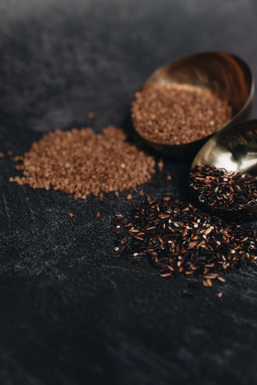Close-up of brown sugar and wild rice grains on a dark surface with a golden scoop.