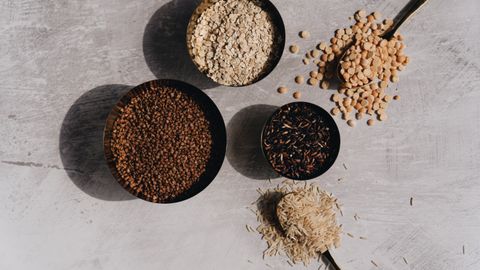 Flat lay of grains and pulses in bowls on a stone surface with shadows, perfect for food-related design.