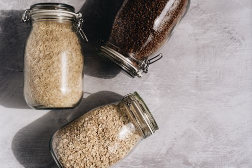 Free Top-down view of rice, oats, and buckwheat in glass jars on a textured surface. Stock Photo