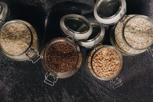 Aerial shot of diverse grains in glass jars showcasing buckwheat, rice, oats, and pulses.