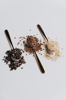 Three types of grains on spoons display variety on a white background, ideal for culinary themes.