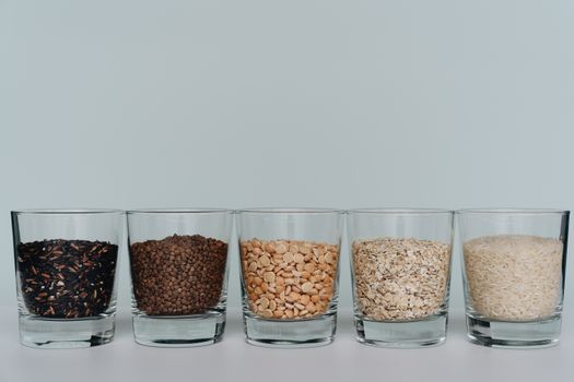 A collection of various grains displayed in clear glasses on a white surface.