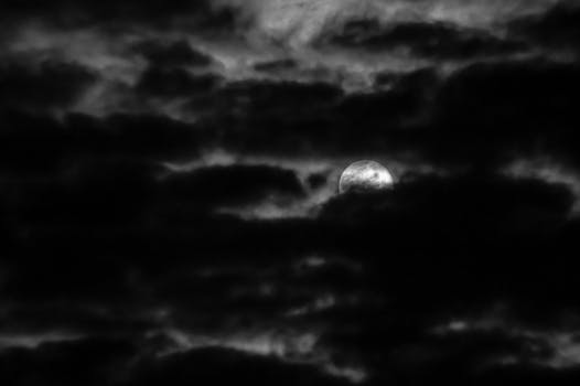 Captivating black and white photo of the moon peeking through dramatic clouds at night.