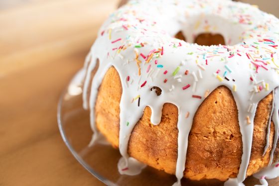 Golden bundt cake covered in thick white icing drips and colorful sprinkles