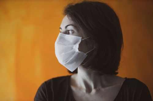 Free A woman wears a protective face mask, looking sideways against an orange background. Stock Photo