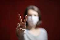 在红色背景下，戴着口罩的人做出和平手势，画面带有柔焦效果