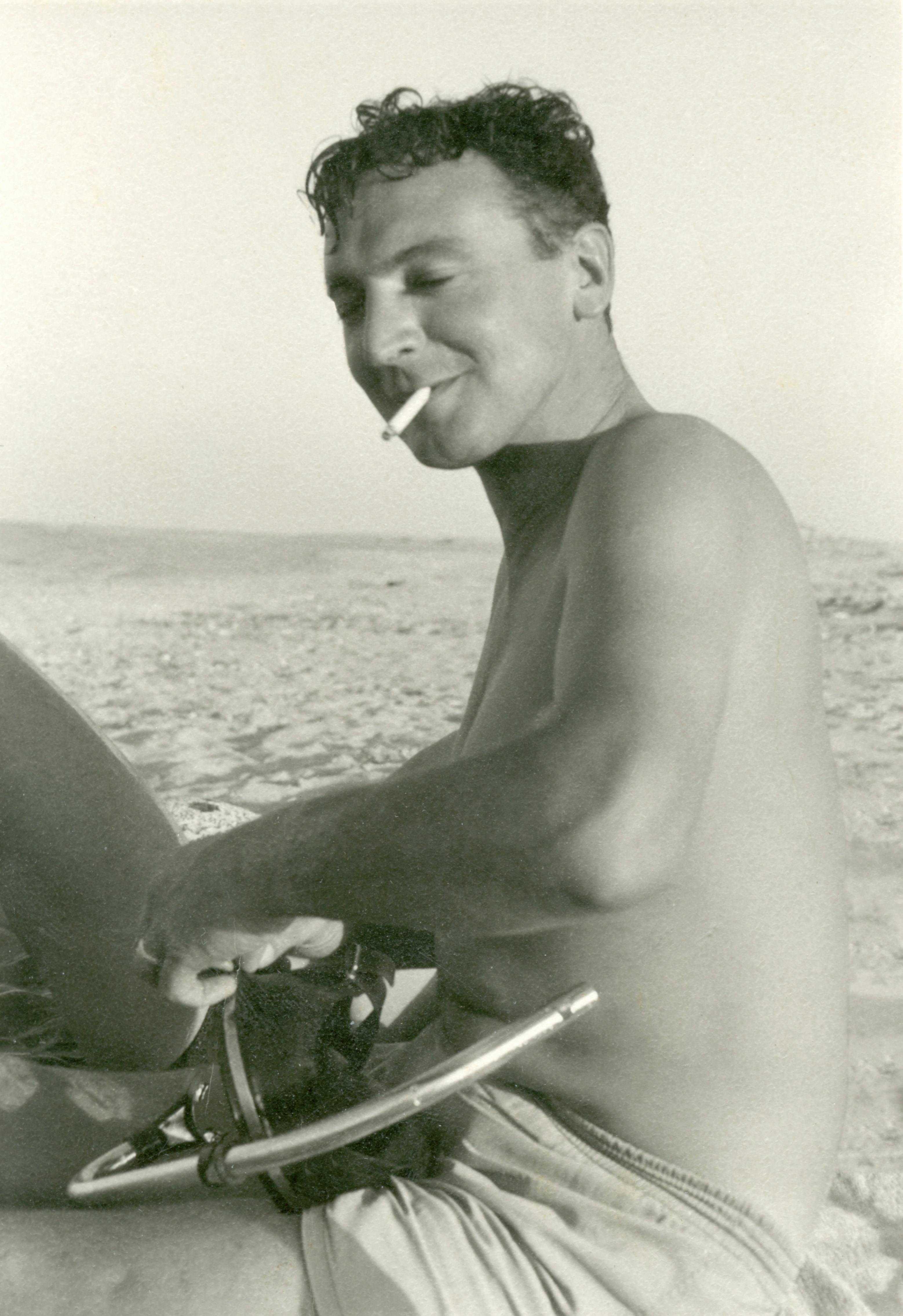 Black and white vintage photo of a shirtless man smoking on the beach.