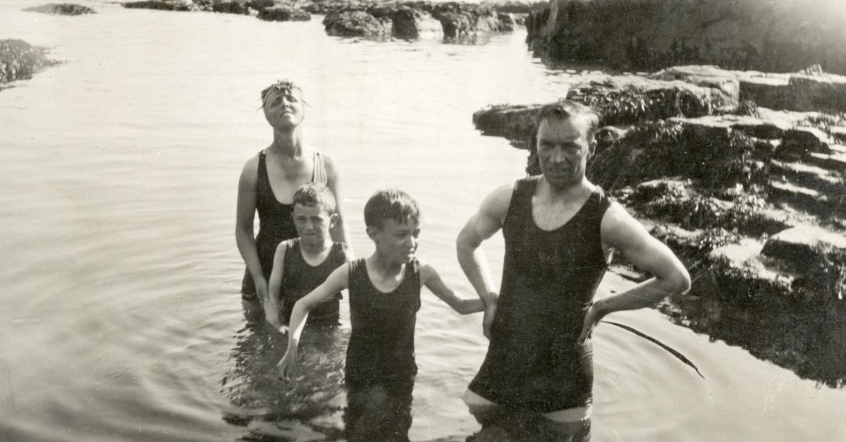 A nostalgic black and white photo of a family swimming at the beach in vintage swimsuits.