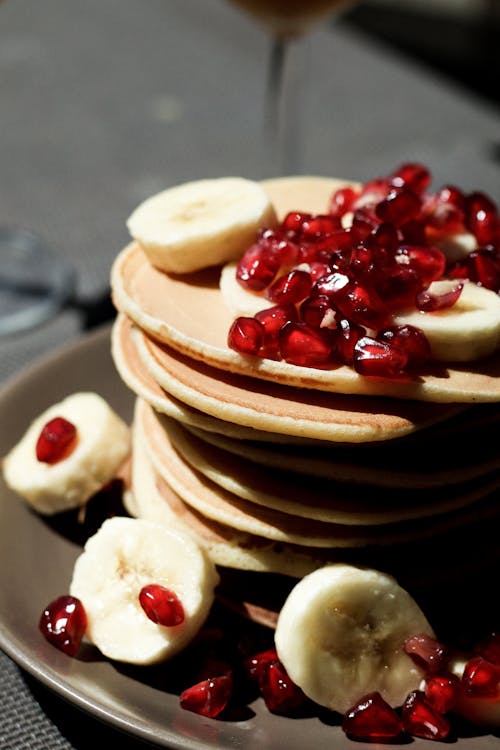 Free From above of tasty homemade pancakes served with fresh red garnet grains and banana Stock Photo