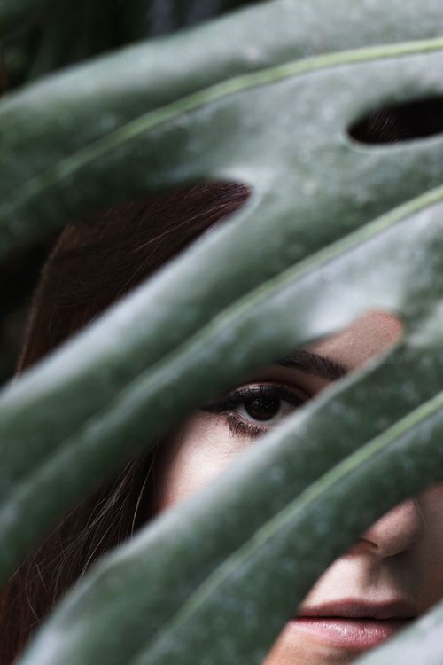 Free Close-up of a woman's eye peering through a tropical leaf. Artistic and mysterious. Stock Photo