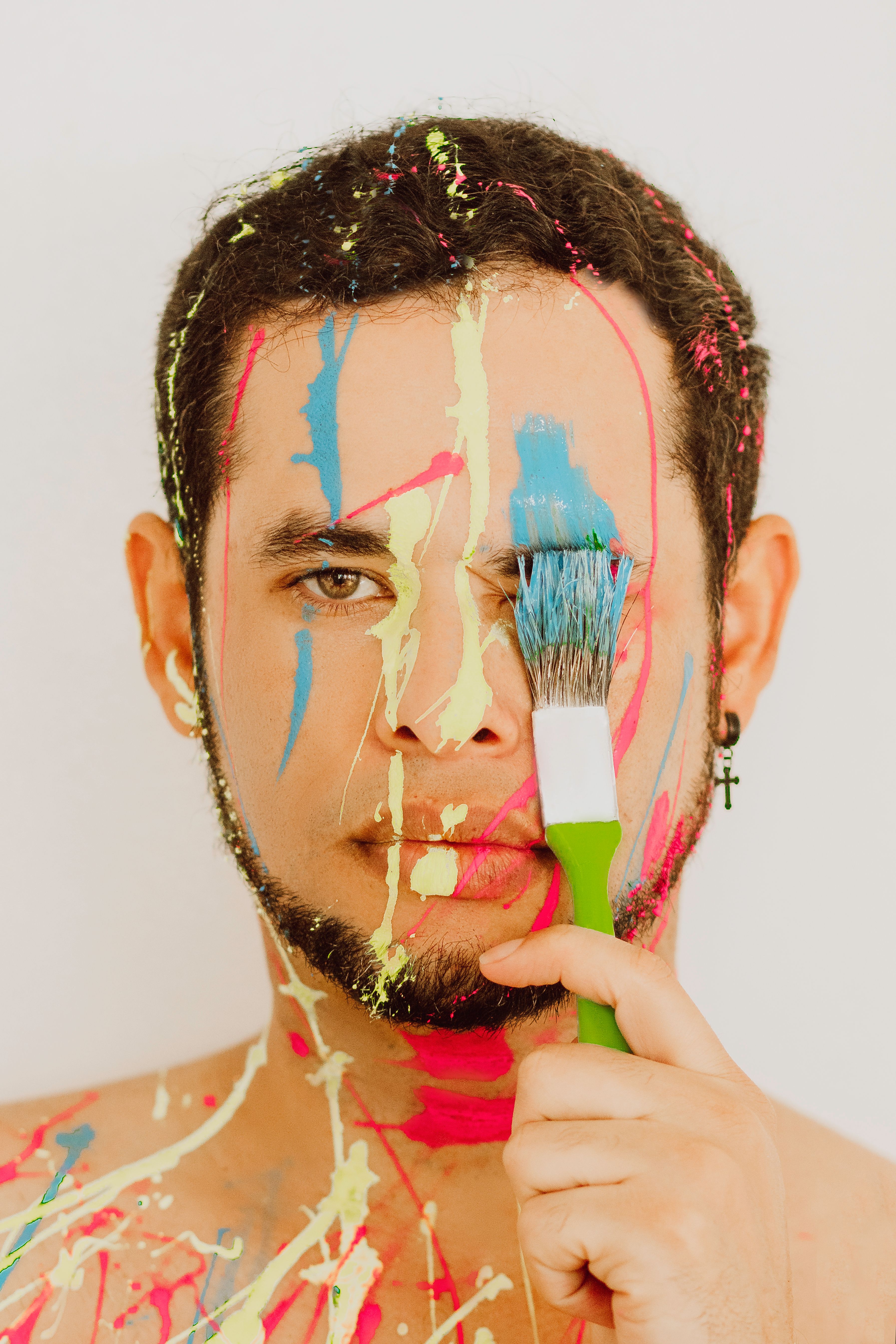 A creative portrait of a man with vibrant paint drips and a brush, showcasing artistic expression.