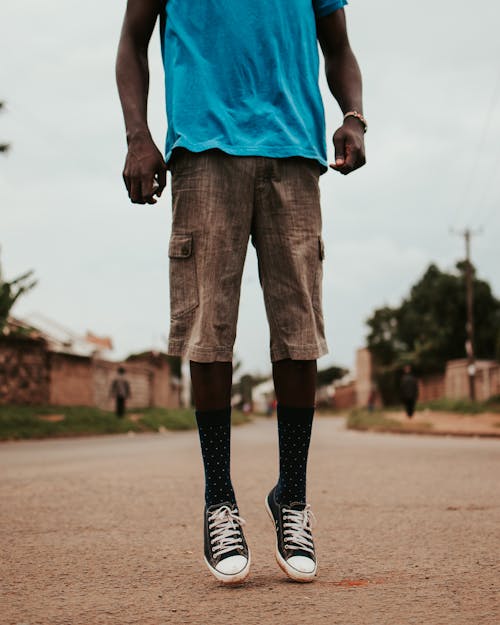 Crop unrecognizable African American male in casual outfit and sneakers jumping on asphalt road