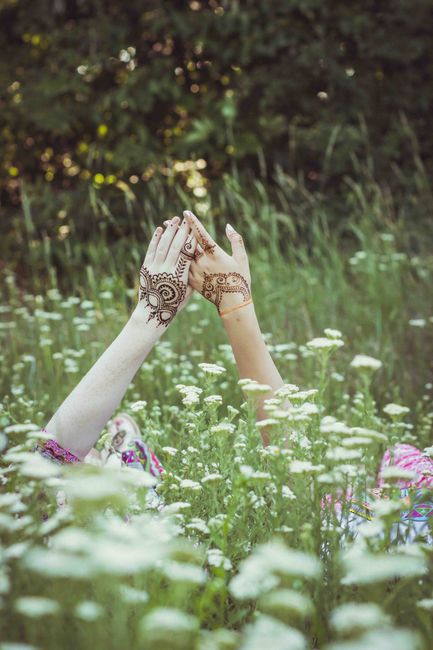 Hands with henna tattoos raised among wildflowers in a serene field setting.