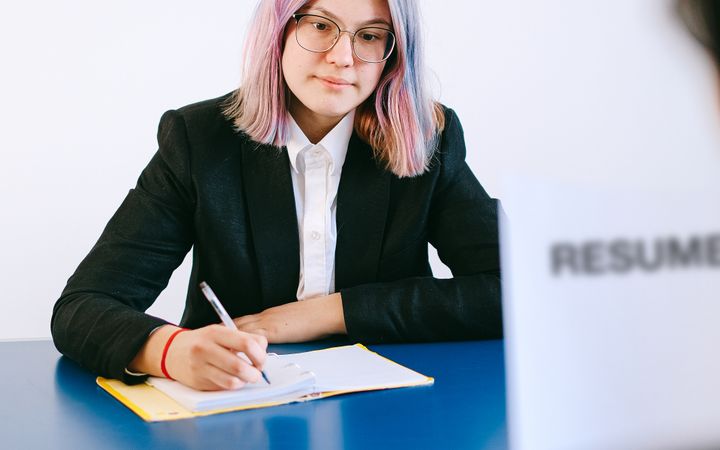 Professional woman with dyed hair taking notes during a job interview.