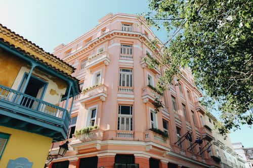 Free Charming pink residential building with elegant balconies and lush greenery in an urban setting. Stock Photo