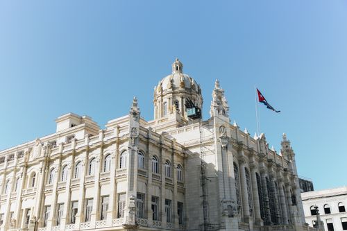Free Stunning architecture of a Cuban government building with national flag waving under a clear blue sky. Stock Photo