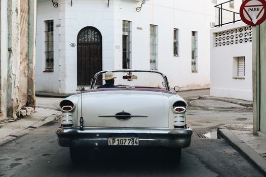 Retro car with driver in a hat cruising through quaint city streets.