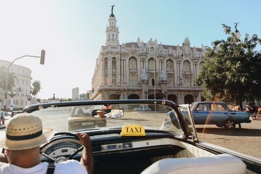 Classic convertible taxi in front of ornate architecture in Havana, Cuba, capturing urban culture.