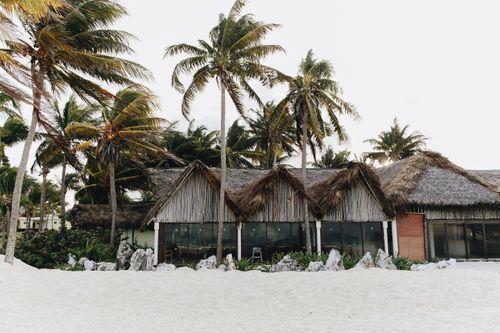 Free Rustic thatched-roof bungalow on a sandy beach surrounded by palm trees. Stock Photo