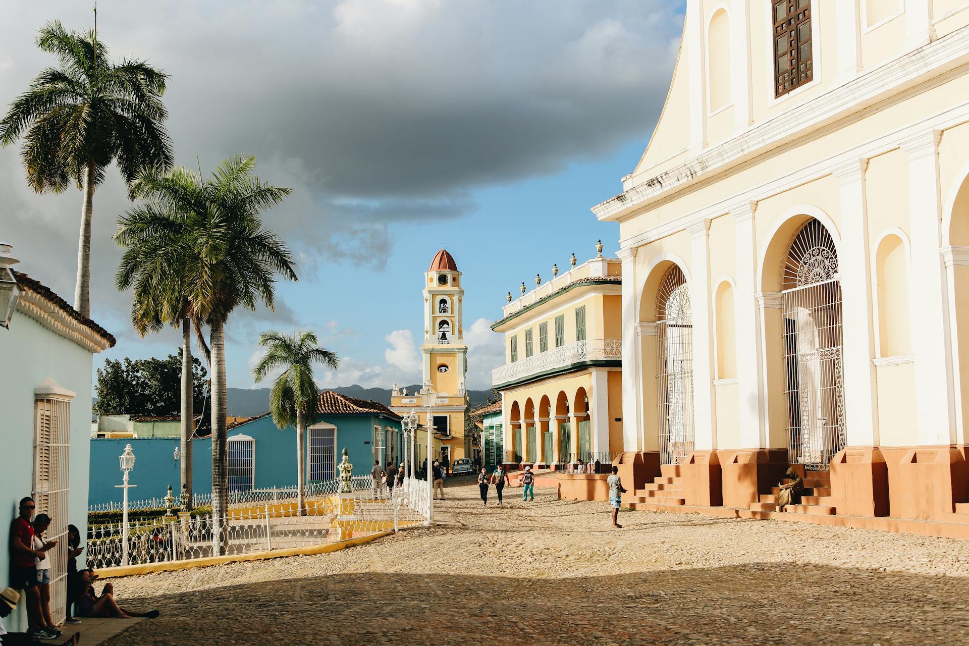 Picturesque colonial town square featuring a church, bell tower, and palm trees.