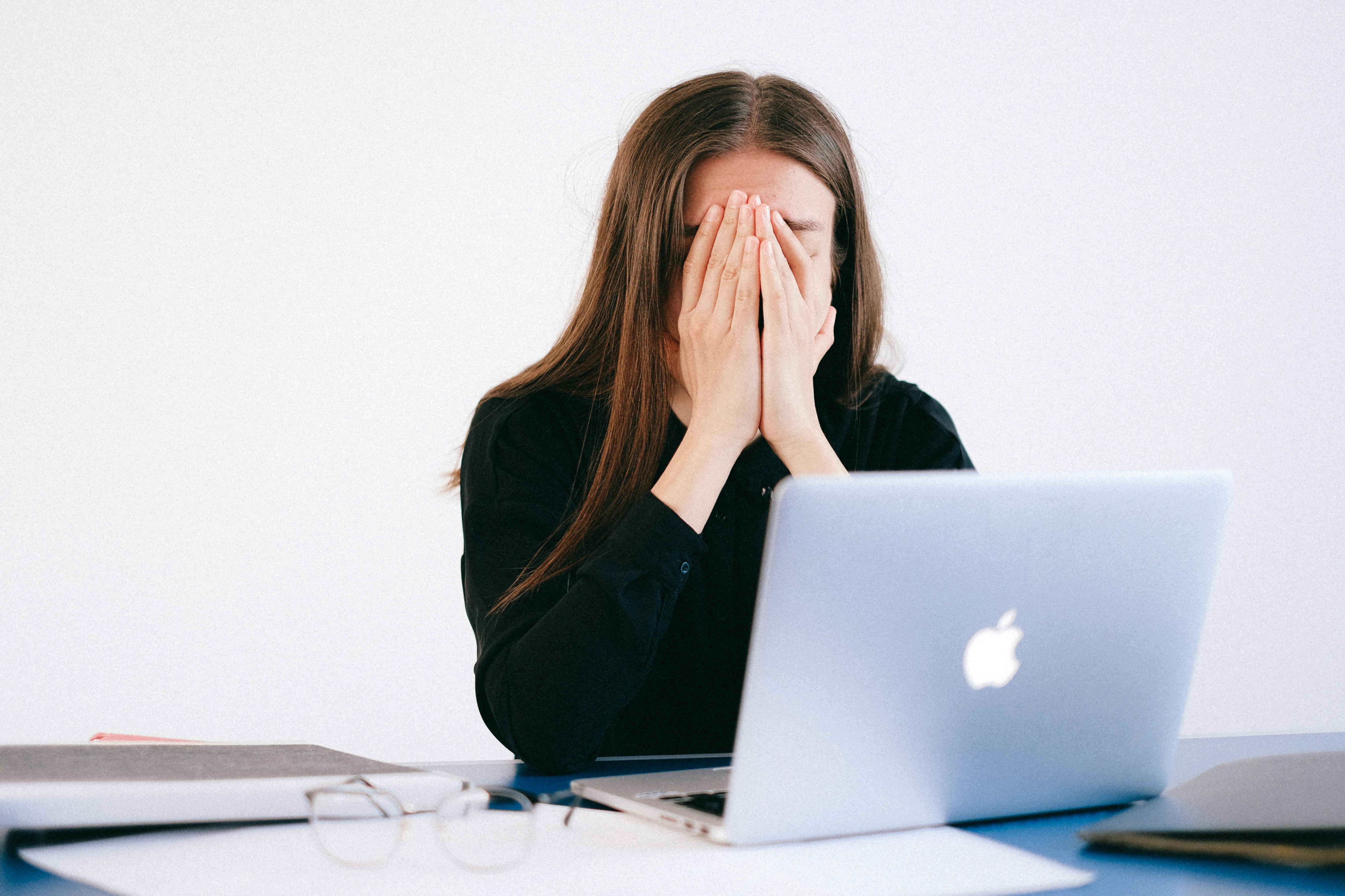 Woman feeling stressed and overwhelmed at her desk while working remotely on a laptop