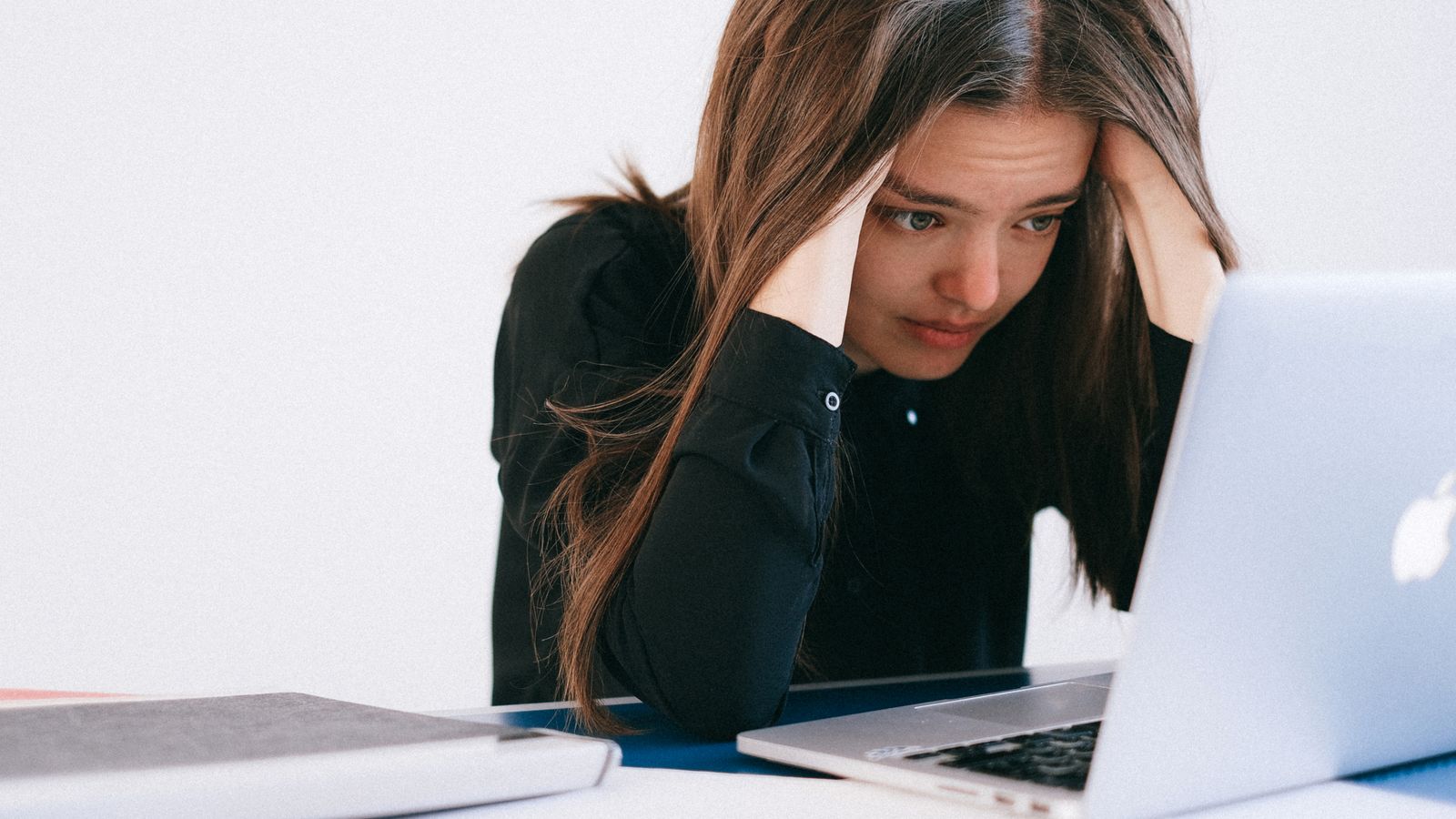 A worried person resting their head in their hands while looking at a laptop.