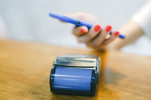 Close-up of hand using smartphone for contactless payment at a terminal on wooden surface.