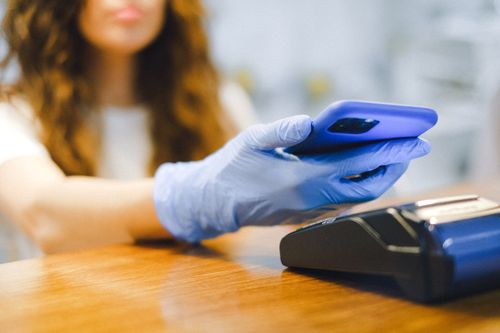 Free Woman using a smartphone for contactless payment in a store while wearing protective gloves. Stock Photo