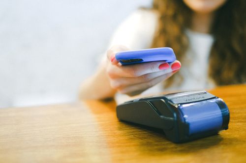 Free Close-up of a woman making a contactless payment using a smartphone over a card reader Stock Photo