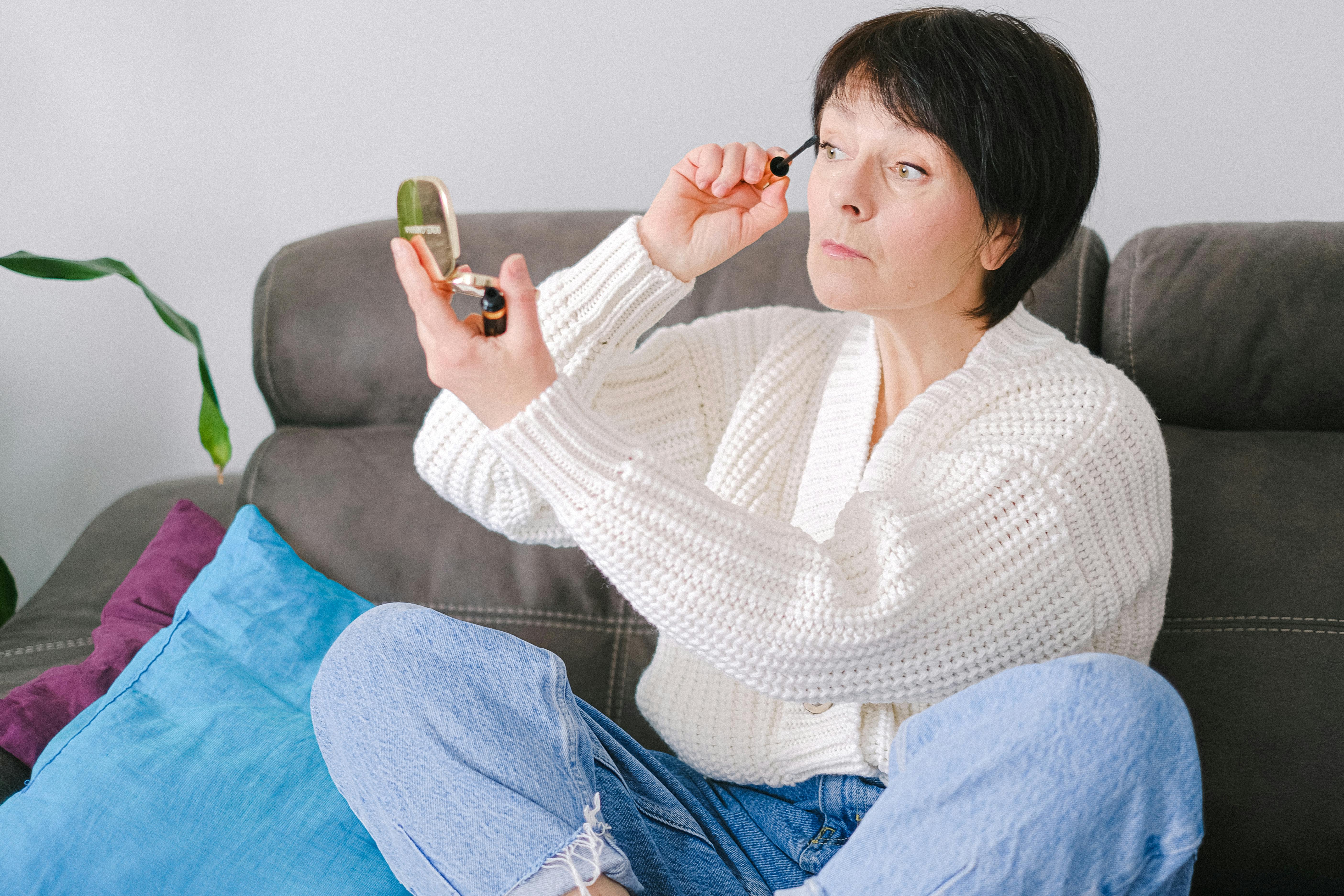 一位白人女性正舒适地坐在沙发上涂着睫毛膏