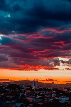 Vibrant evening sky covered with dark blue and pink clouds above houses in town and mountain on horizon