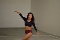 一位年轻苗条的女性，穿着黑色露脐上衣和紫色内衣，在明亮简洁的工作室里练习时，双手伸展，露出灿烂的笑容，目光望向别处