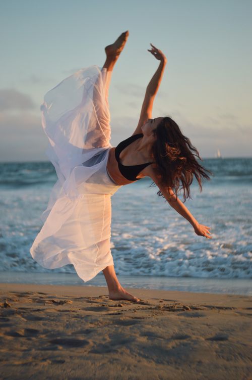 Free Full body of concentrated female dancer in black bra and white long flying skirt outstretching leg and looking up while rehearsing Stock Photo