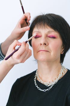 Close-up of a senior woman getting her eyeshadow applied by a makeup artist.