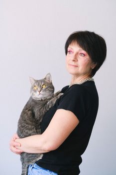 一位妆容鲜艳的优雅女性，在中性背景下抱着虎斑猫摆出姿势